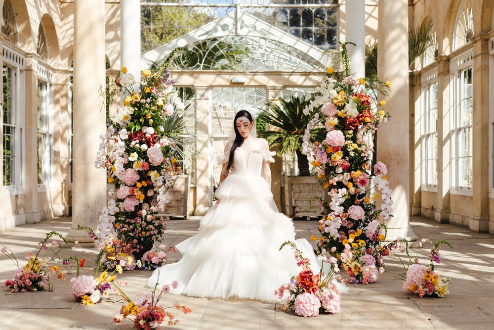 Bride in white gown poses in conservatory with elaborate floral arch installations.