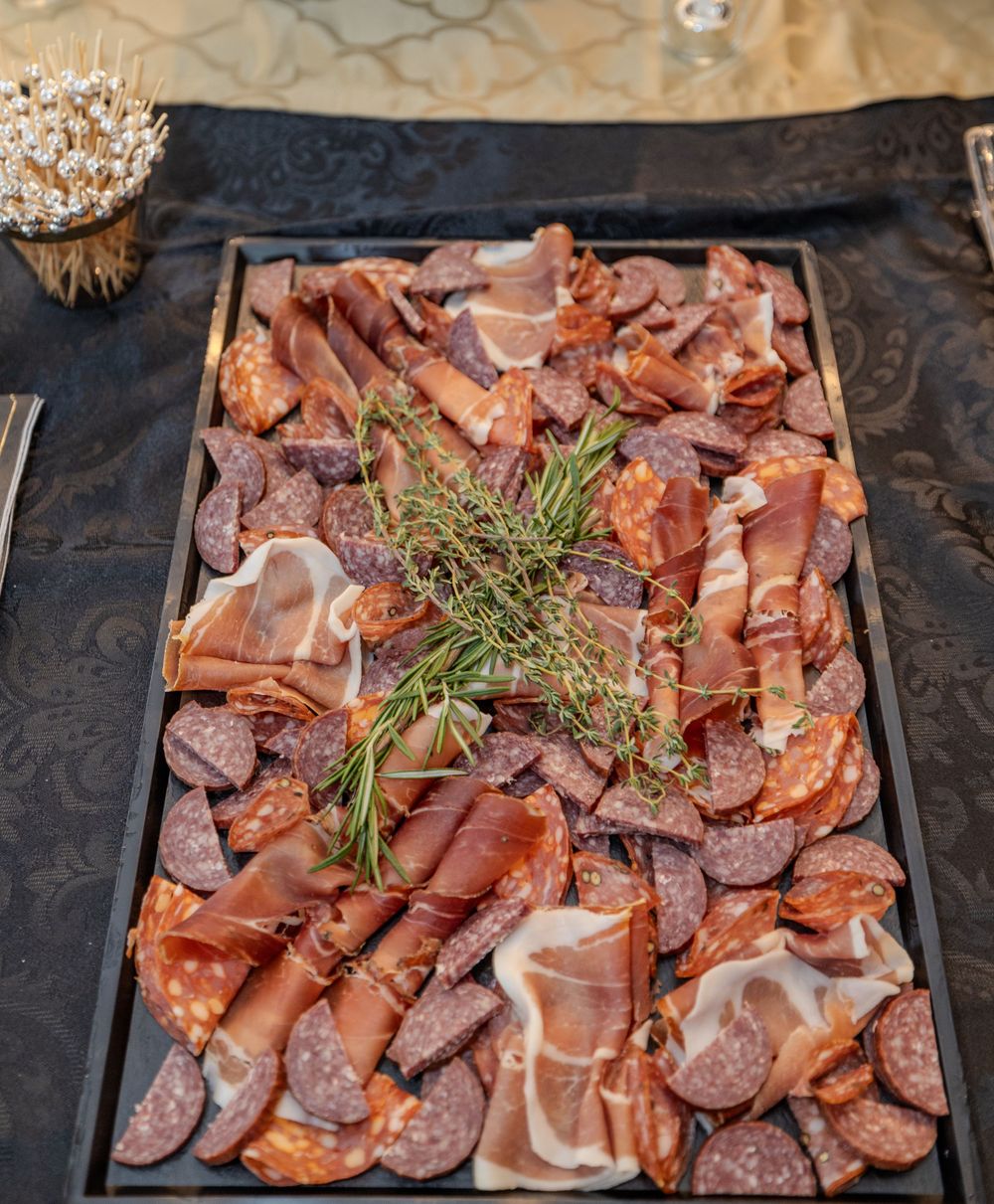 Charcuterie board featuring assorted meats and herbs served on black tablecloth.