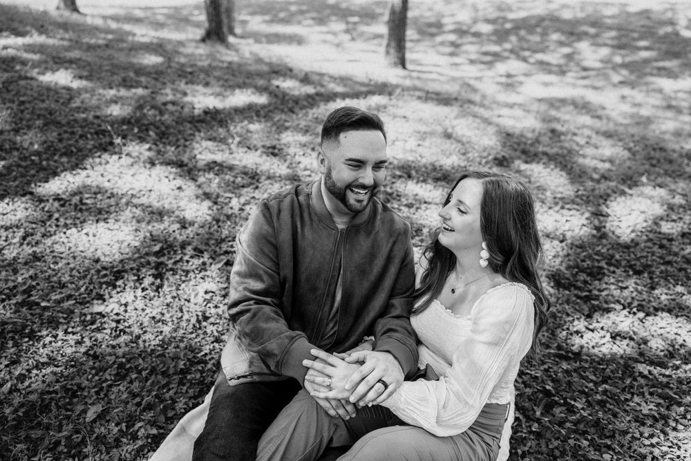 Black and white photo of a happy couple sitting together and laughing in a park.