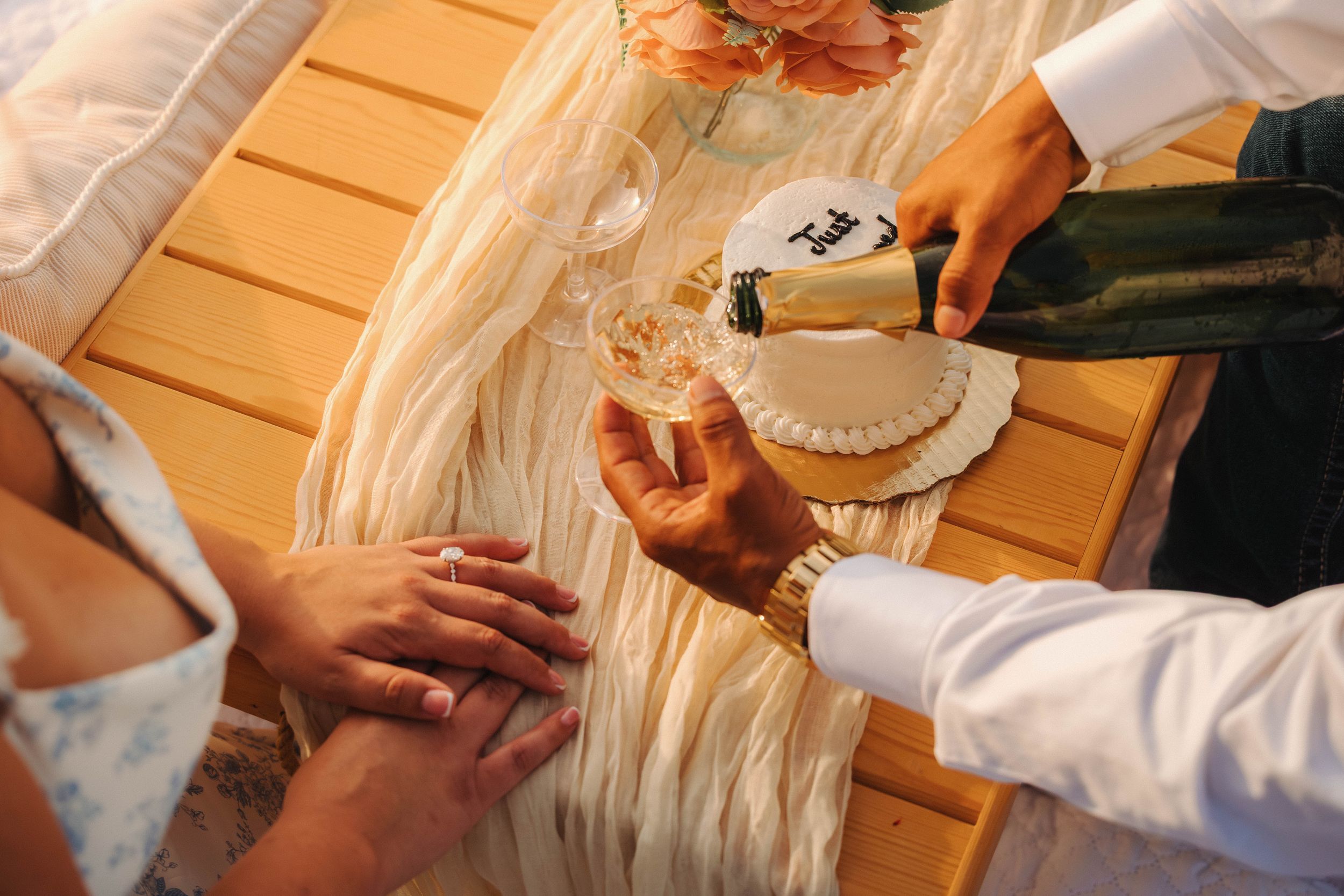 Person pouring champagne into a glass at an elegant outdoor wedding celebration on a wooden table.