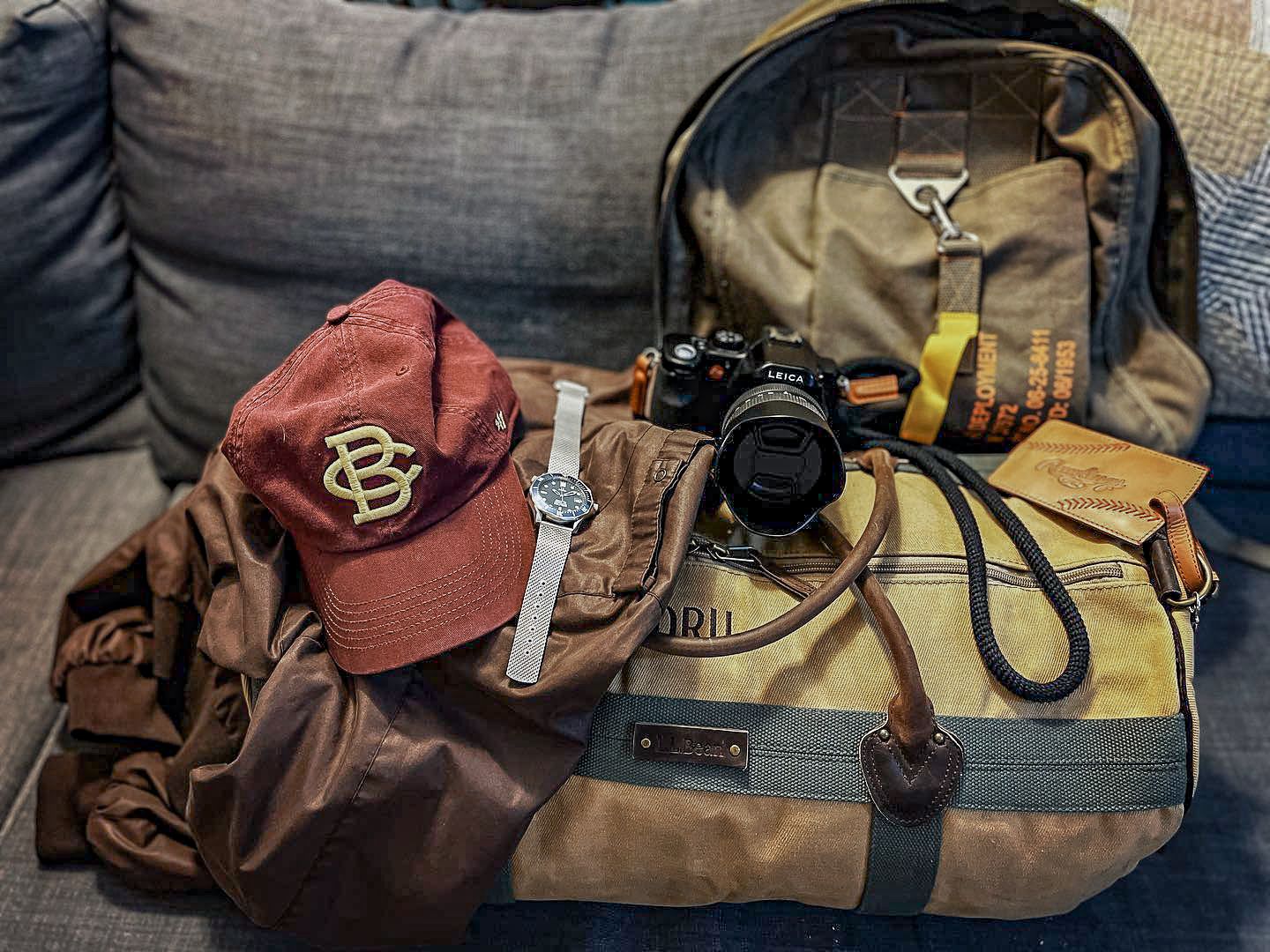Travel gear and camera equipment arranged on a couch with backpack and baseball cap.