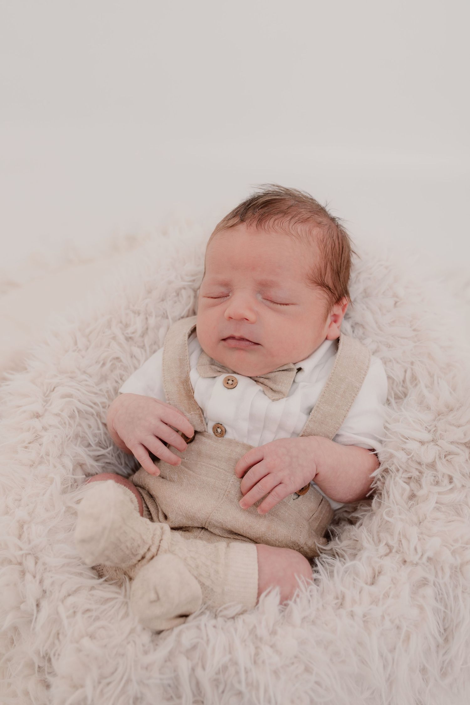 Sleeping newborn baby wearing beige outfit on soft white textured blanket. Photographer. Hull. East Yorkshire. Photography