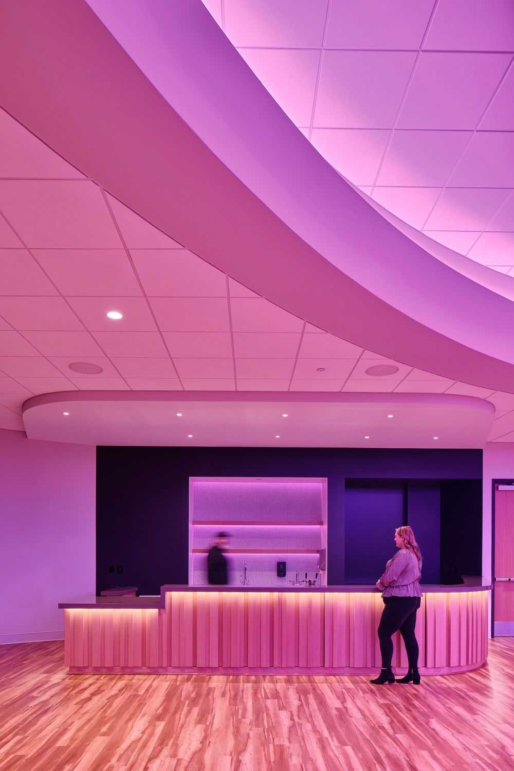 Pink-lit reception area with curved ceiling details and wooden flooring in contemporary commercial space.