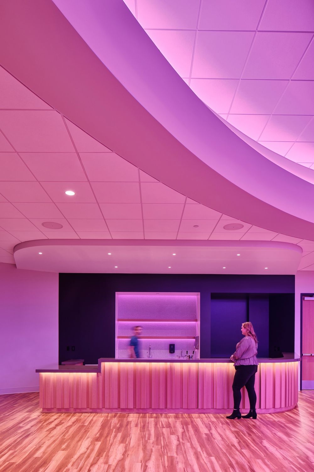 Modern reception counter bathed in pink lighting with curved architectural ceiling elements.