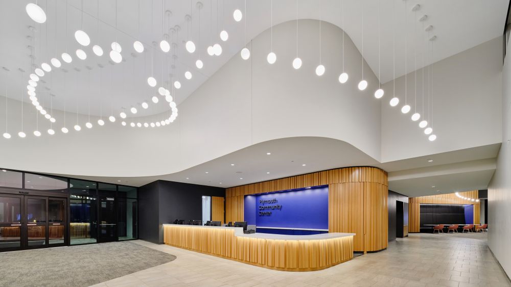 Modern reception area with curved wooden desk and decorative ceiling lighting pattern.