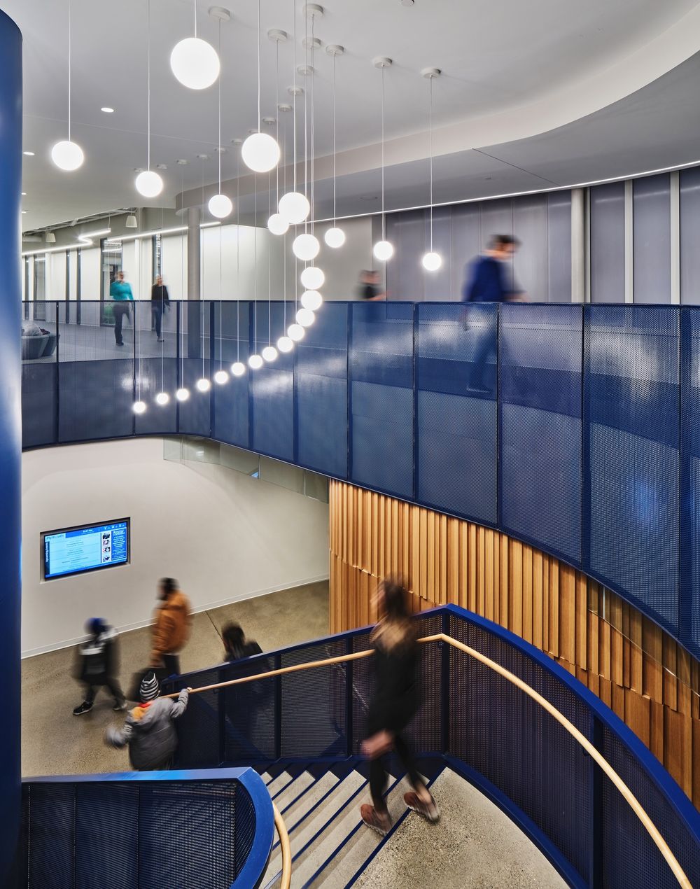Curved stairwell with floating globe lights and blue panels creates dynamic movement in modern office space.