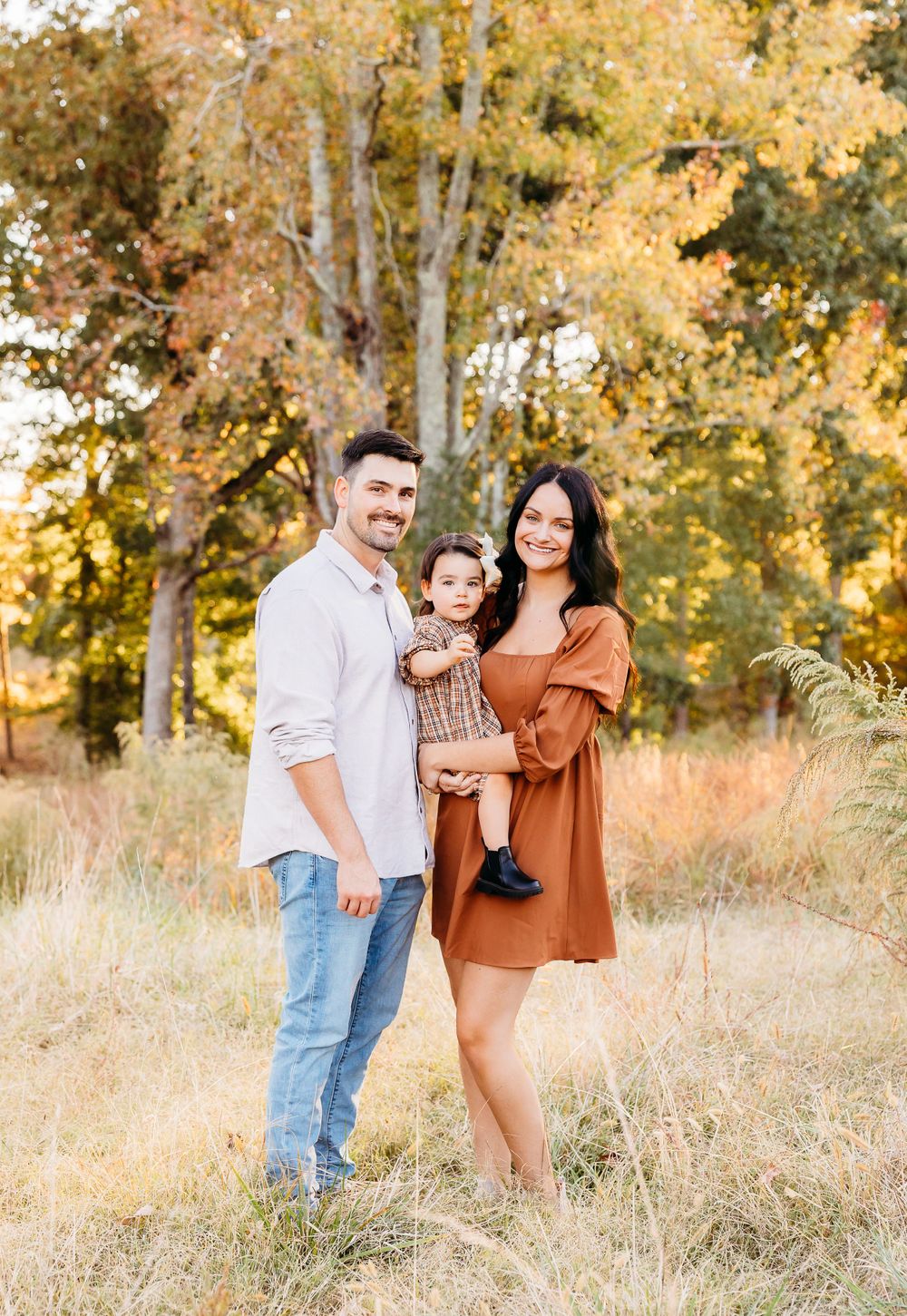 A family enjoying a warm autumn day together in a golden field with tall grass and trees in the background.