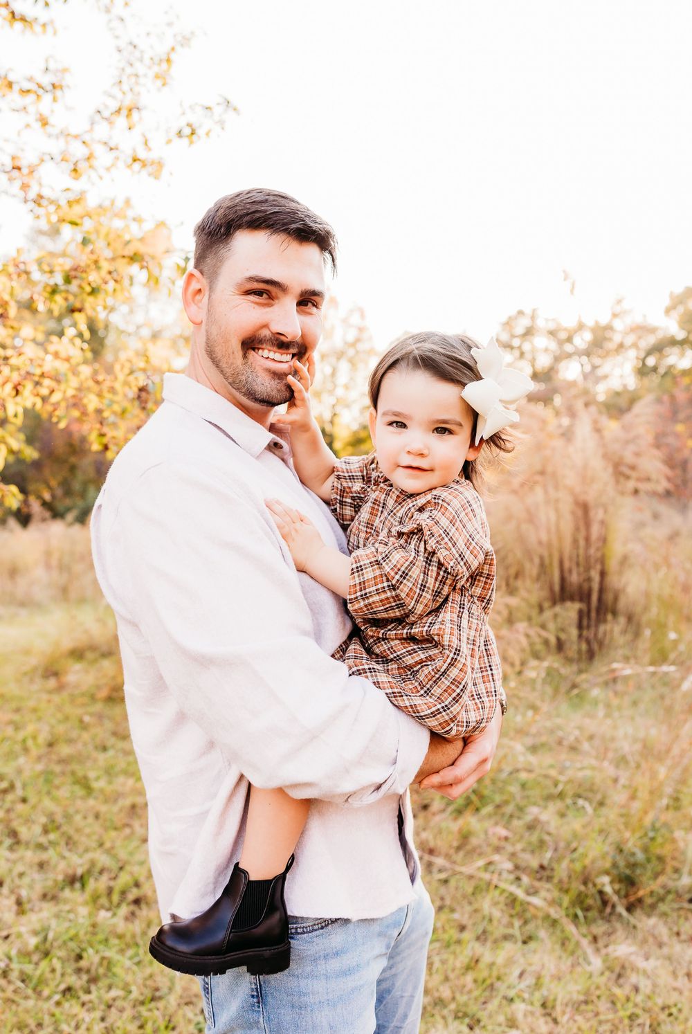 A parent and child share joyful moments in a sun-drenched autumn field during a casual outdoor photoshoot.