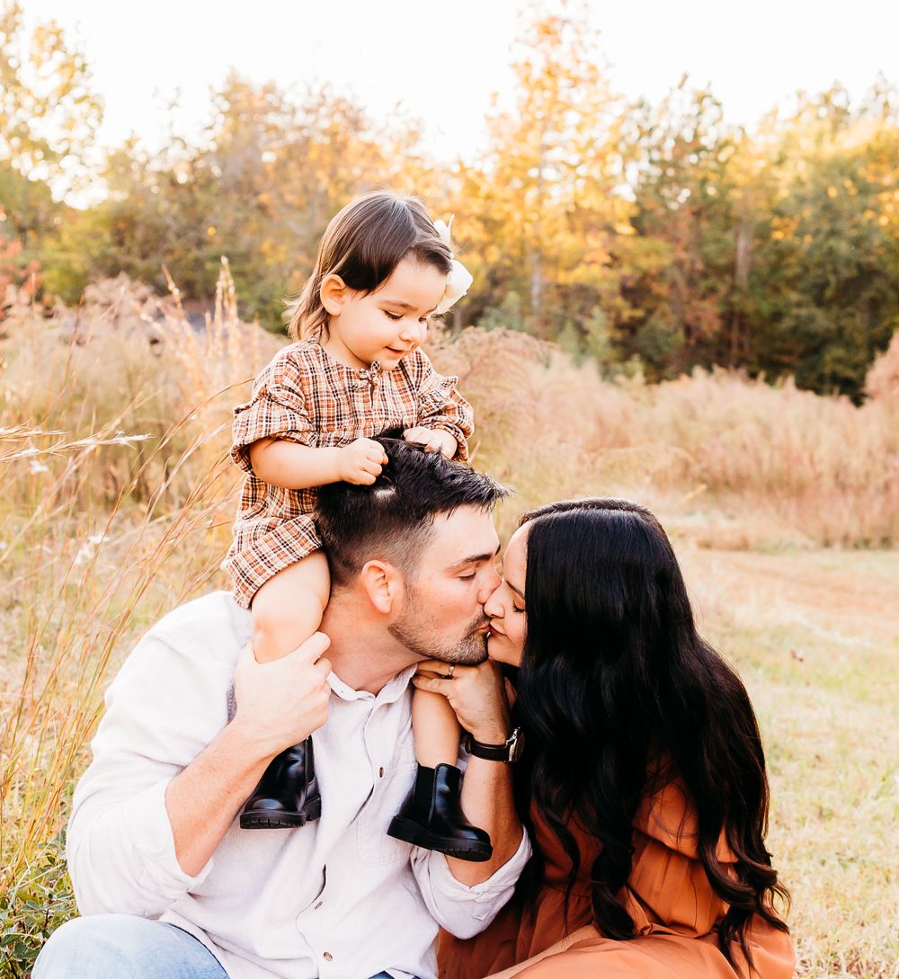 A family shares a tender moment together while sitting in a golden autumn field at sunset.