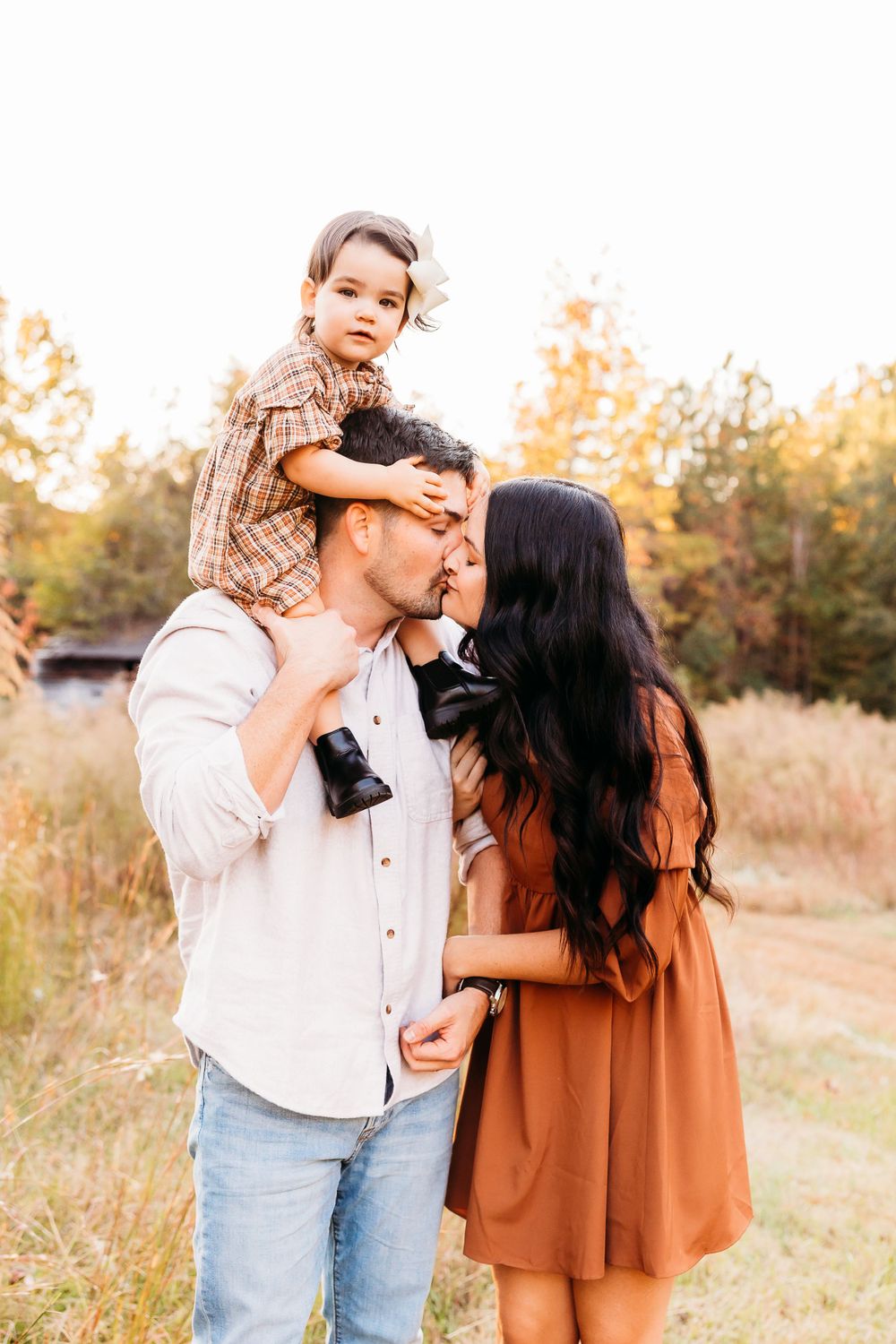 A couple shares tender moments in a golden field during sunset while wearing casual fall attire.