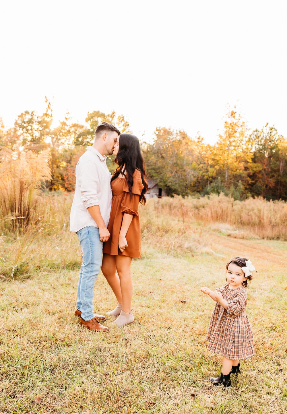 A family shares tender moments in a golden sunlit field during an autumn photoshoot at sunset.