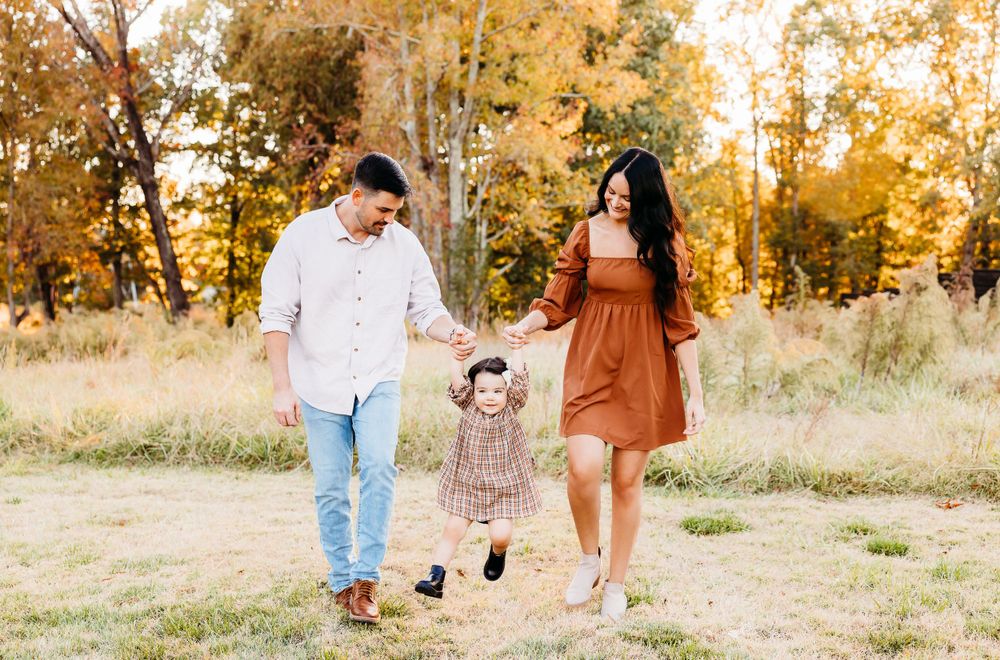 A family walking together in a golden autumn field during sunset, holding hands and enjoying the warm light.