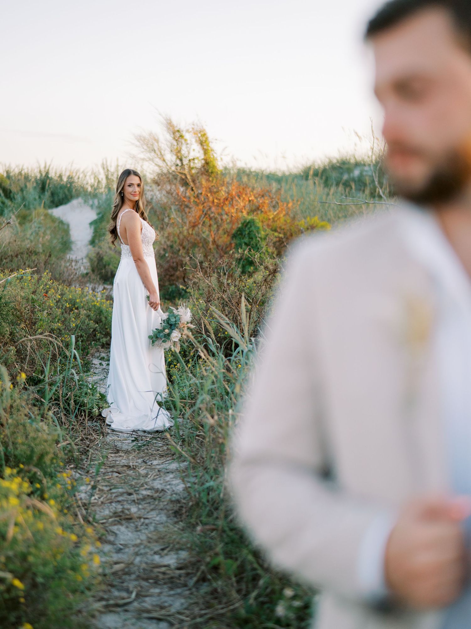 Couple in wedding attire posing on nature path with autumn foliage.