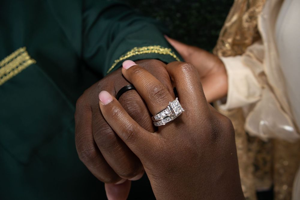 Close-up of a woman's hand wearing a diamond engagement ring held by a man's hand at a wedding ceremony.