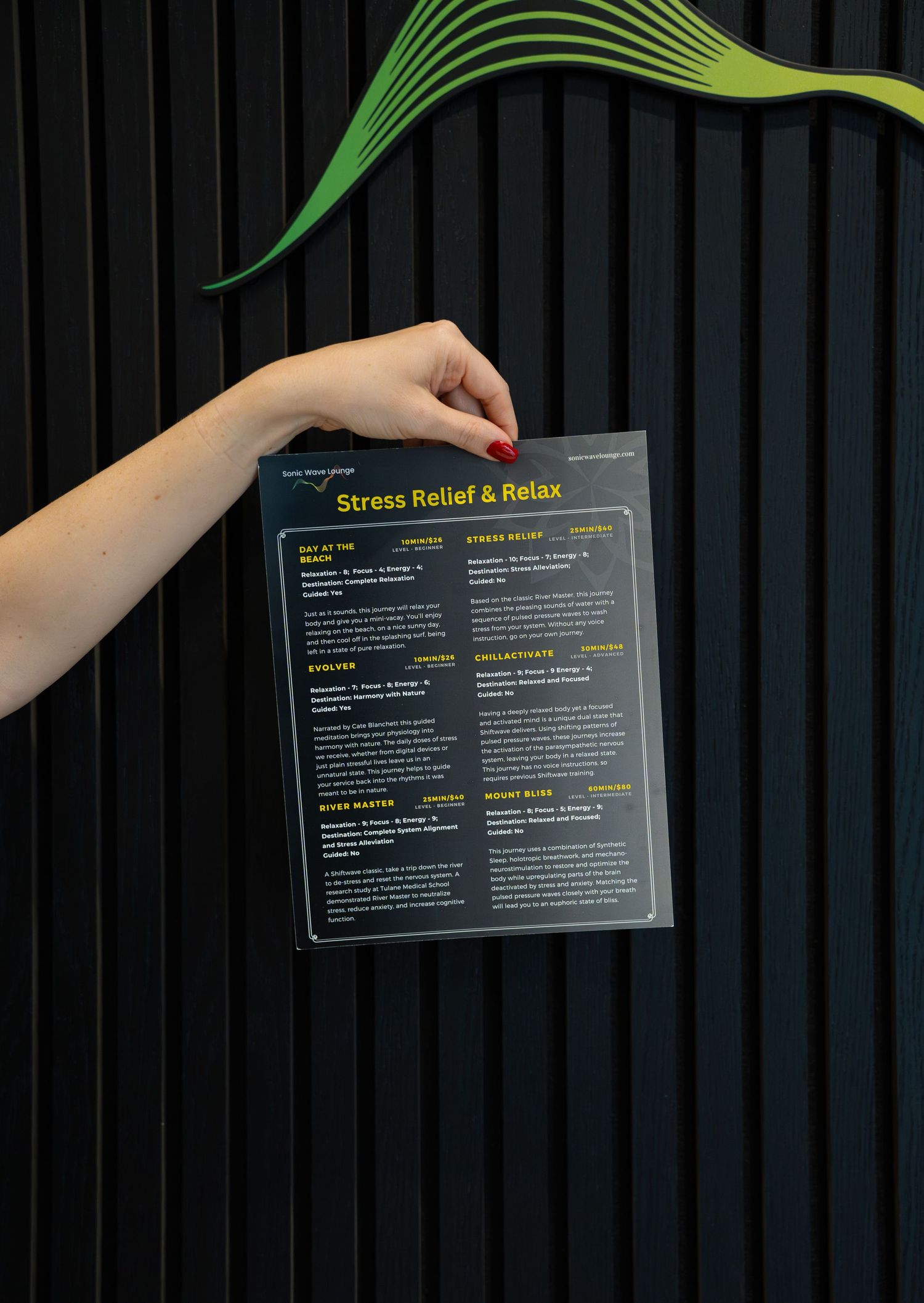 Hand holding stress relief and relax menu against black paneled wall with green wave design.