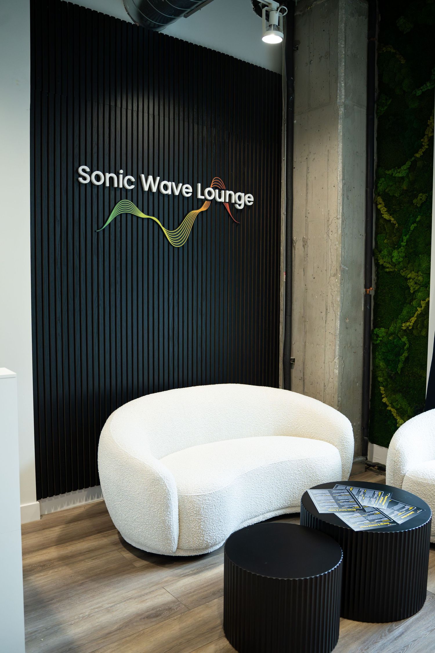 Modern lounge area with curved white sofa and Sonic Wave Lounge branding on black wall.