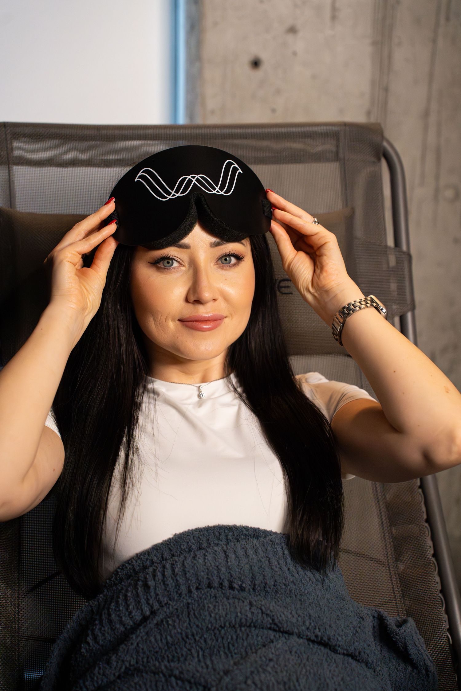 Relaxing client wearing a black sleep mask with wave design and white t-shirt in a reclining chair.