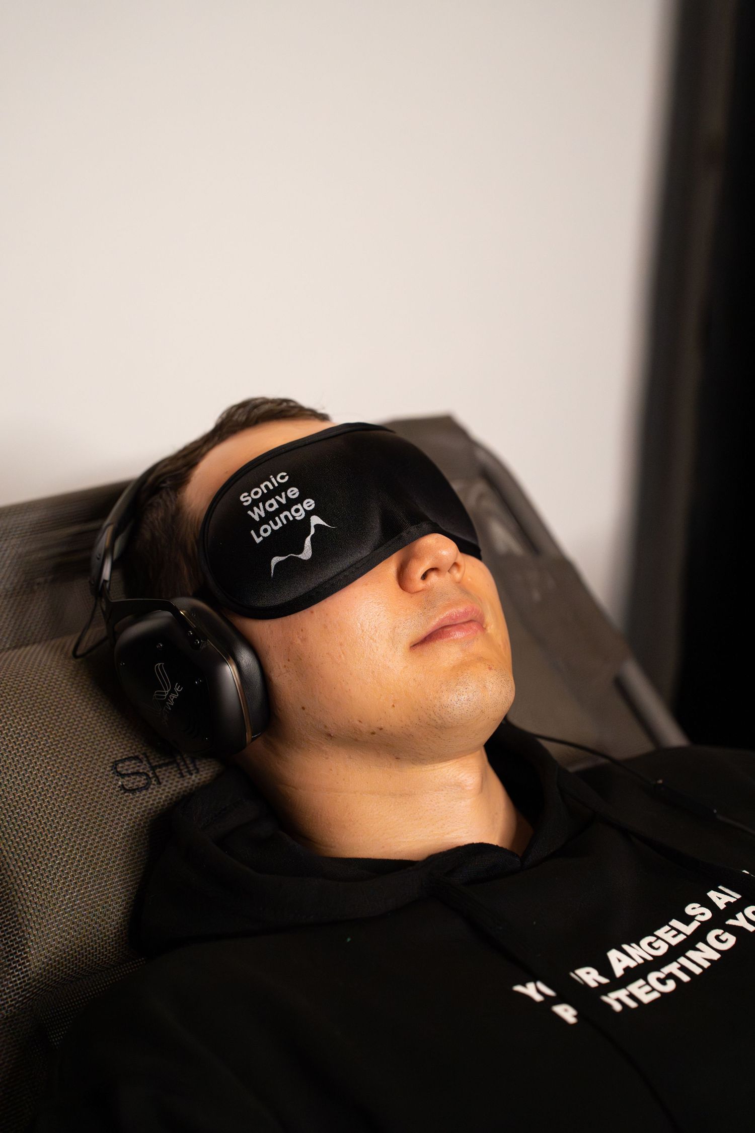 Person wearing black sleep mask and headphones while reclining in a chair.