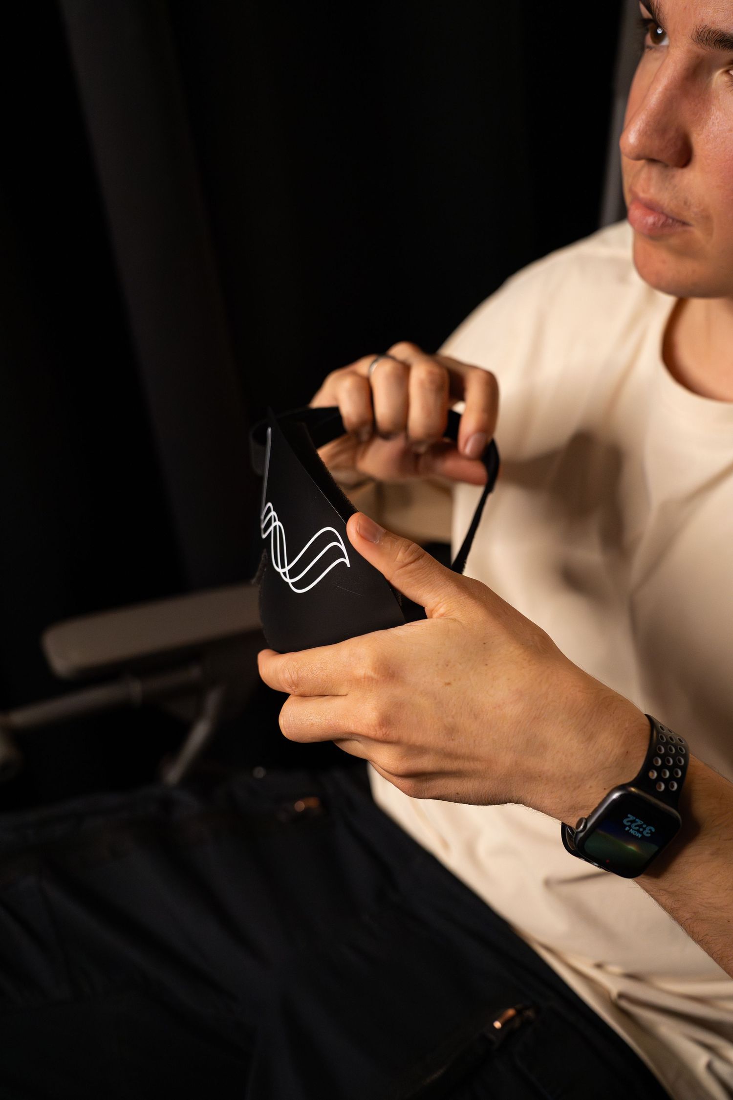 Person in white t-shirt holding a black device with Wave logo while wearing smartwatch.