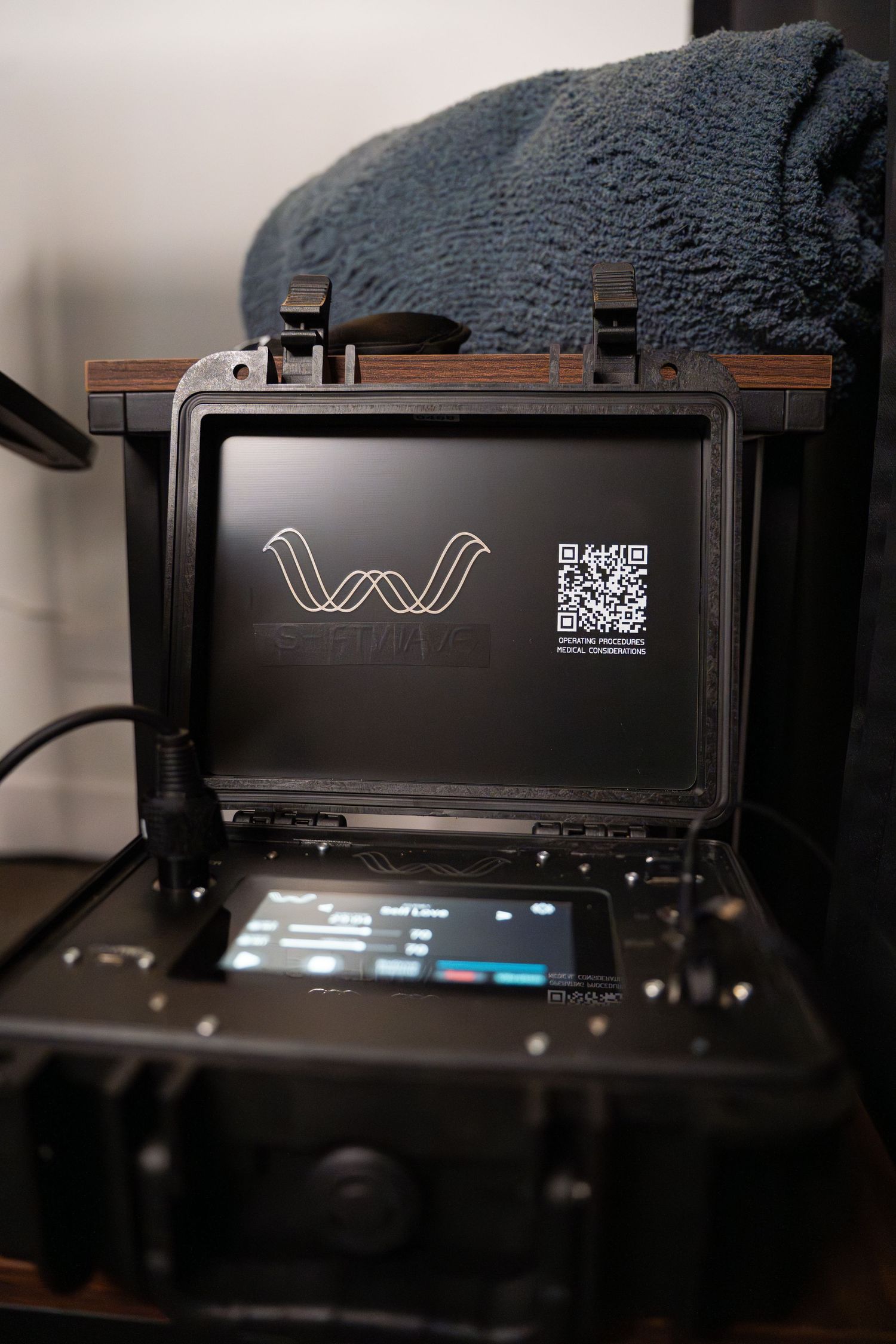 Black digital display device showing a wavy logo and QR code on screen.