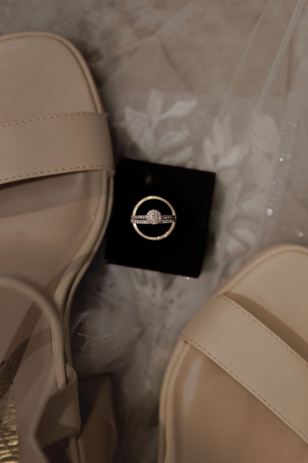 Wedding ring displayed on black velvet between beige sandals in elegant styling shot.