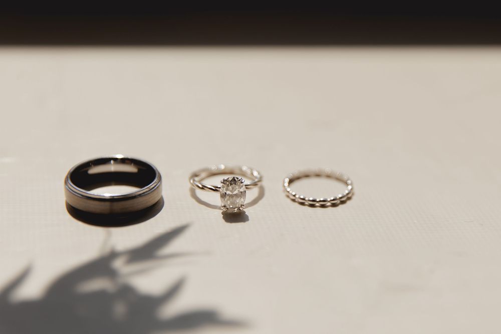 Three wedding rings including a black band, diamond solitaire, and eternity band arranged on white surface with shadow.