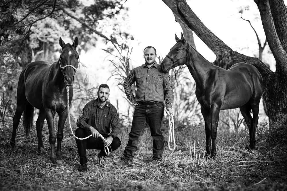 A black and white photograph of people with two horses in a natural outdoor setting among trees.