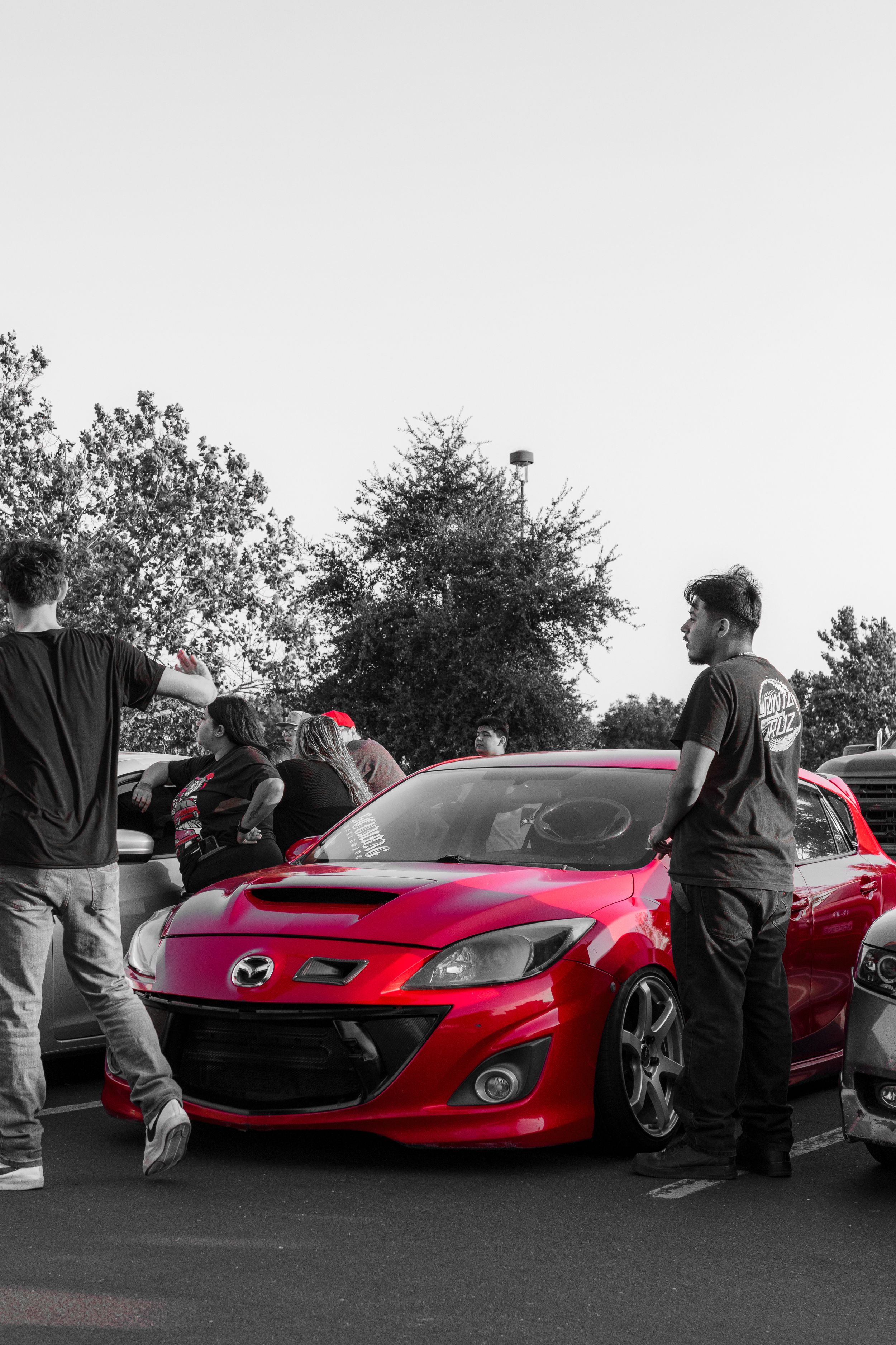 Red Mazda sports car surrounded by people at an outdoor car meet event.