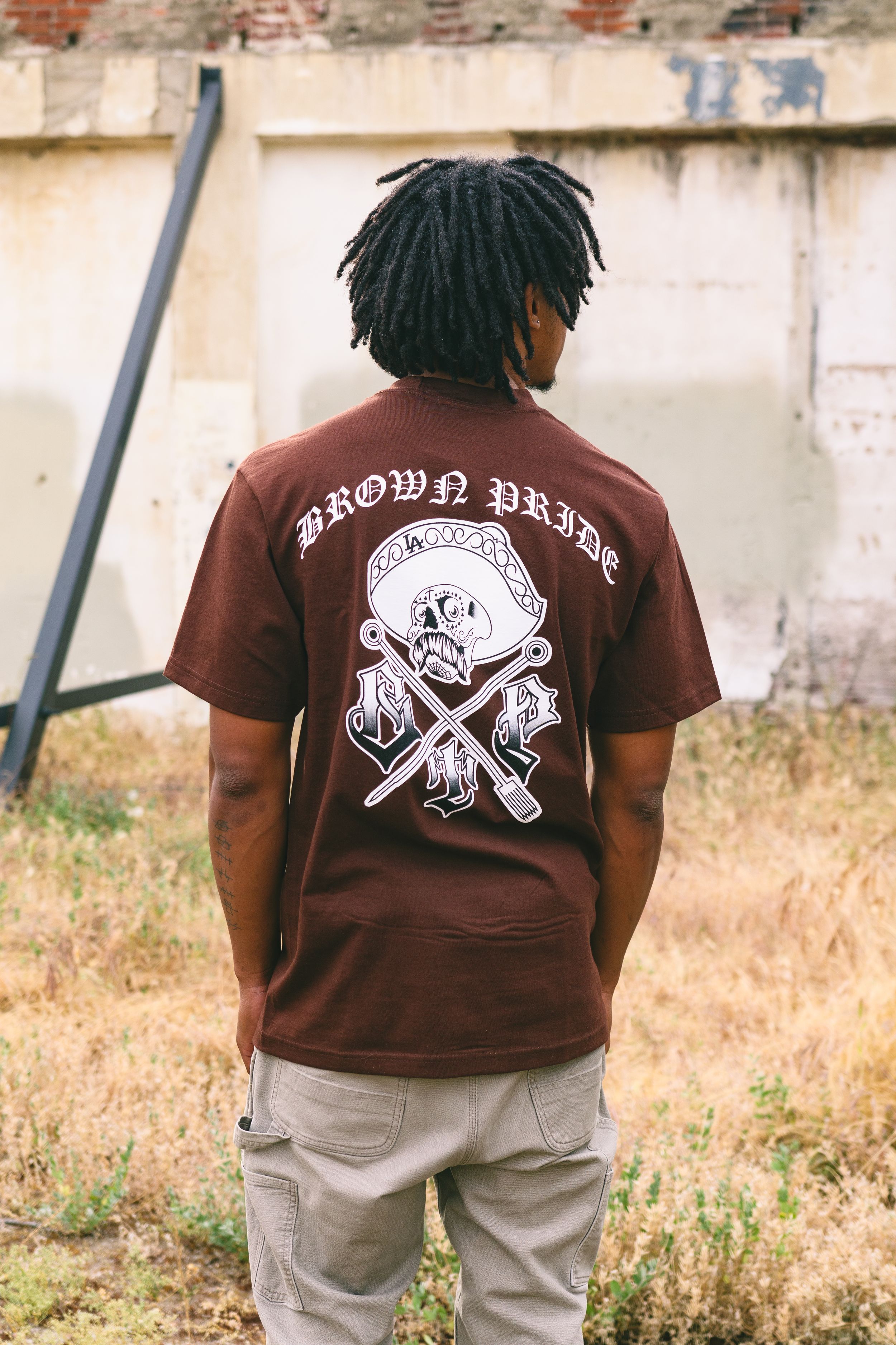 Man wearing a brown Pride graphic t-shirt with skull design standing outdoors.