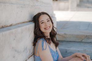 A person in a blue dress laughs joyfully while posing on a sunny concrete staircase.