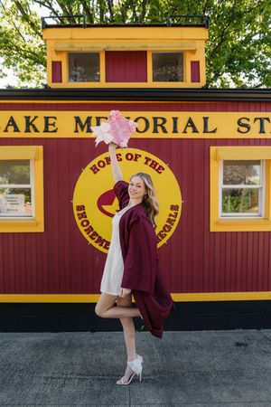 A burgundy gown and white dress ensemble photographed in front of a red and yellow train car memorial store.