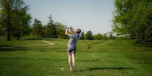 Golf player following through on a swing on a lush green fairway with trees lining the course.