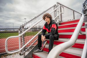 A figure sits on red and white stadium bleachers in casual clothing on an overcast day.