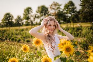 Woman lying in a sunflower field on a sunny summer day surrounded by bright yellow blooms and green foliage.