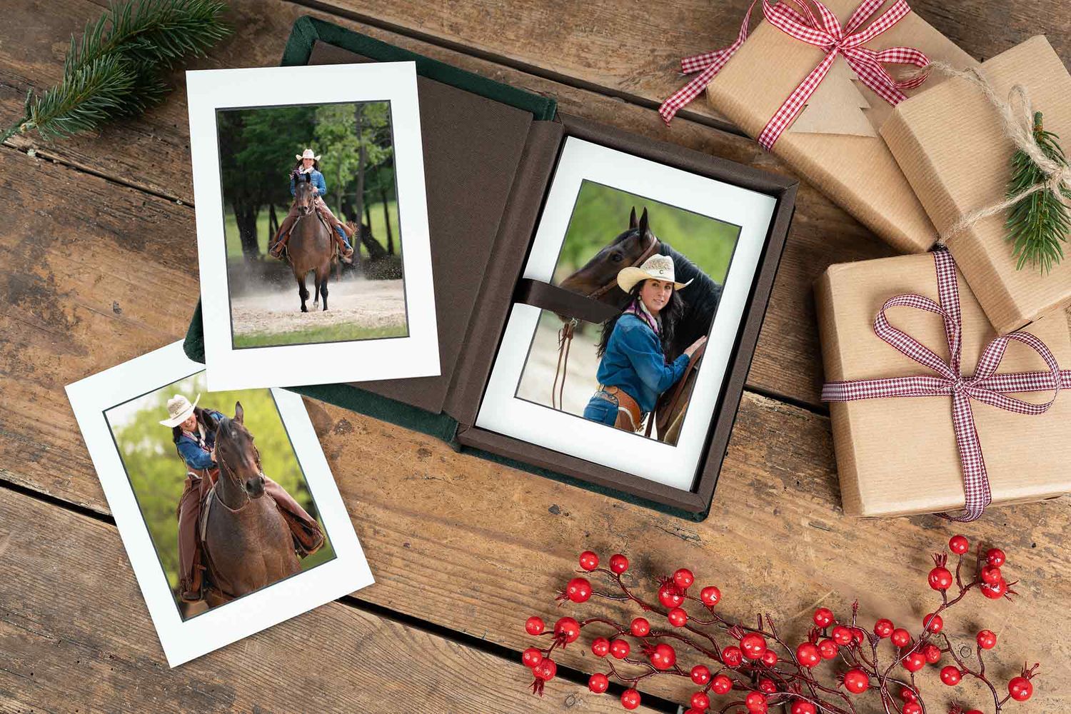 Holiday flatlay with equestrian photos, wrapped presents, pine branches and red berries on rustic wooden table.