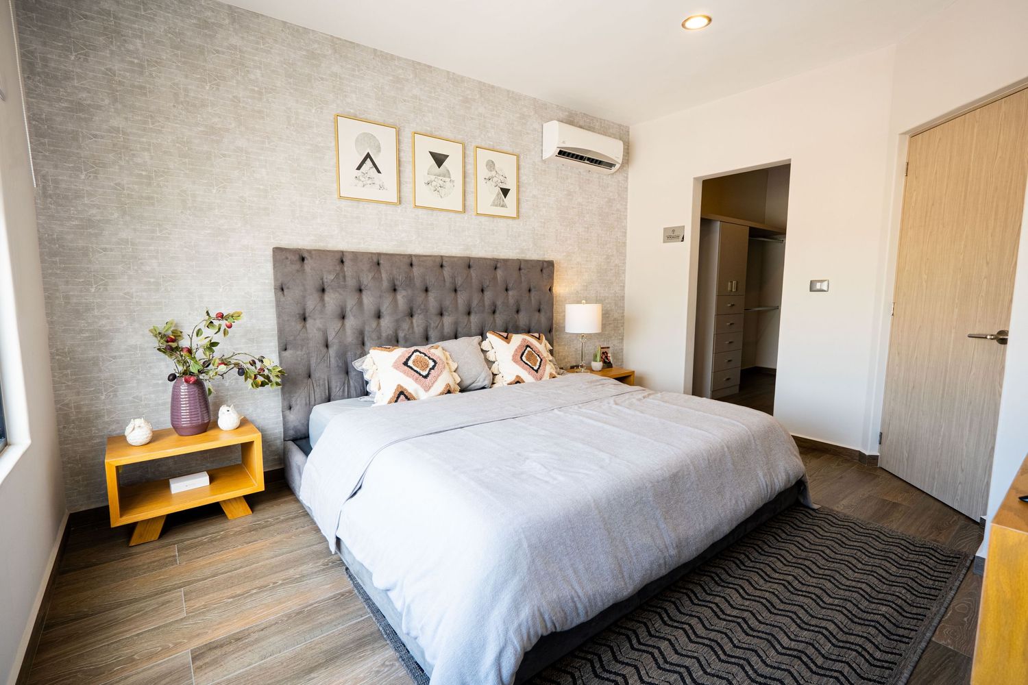 Modern bedroom interior with grey upholstered headboard, white bedding and minimalist wall art.