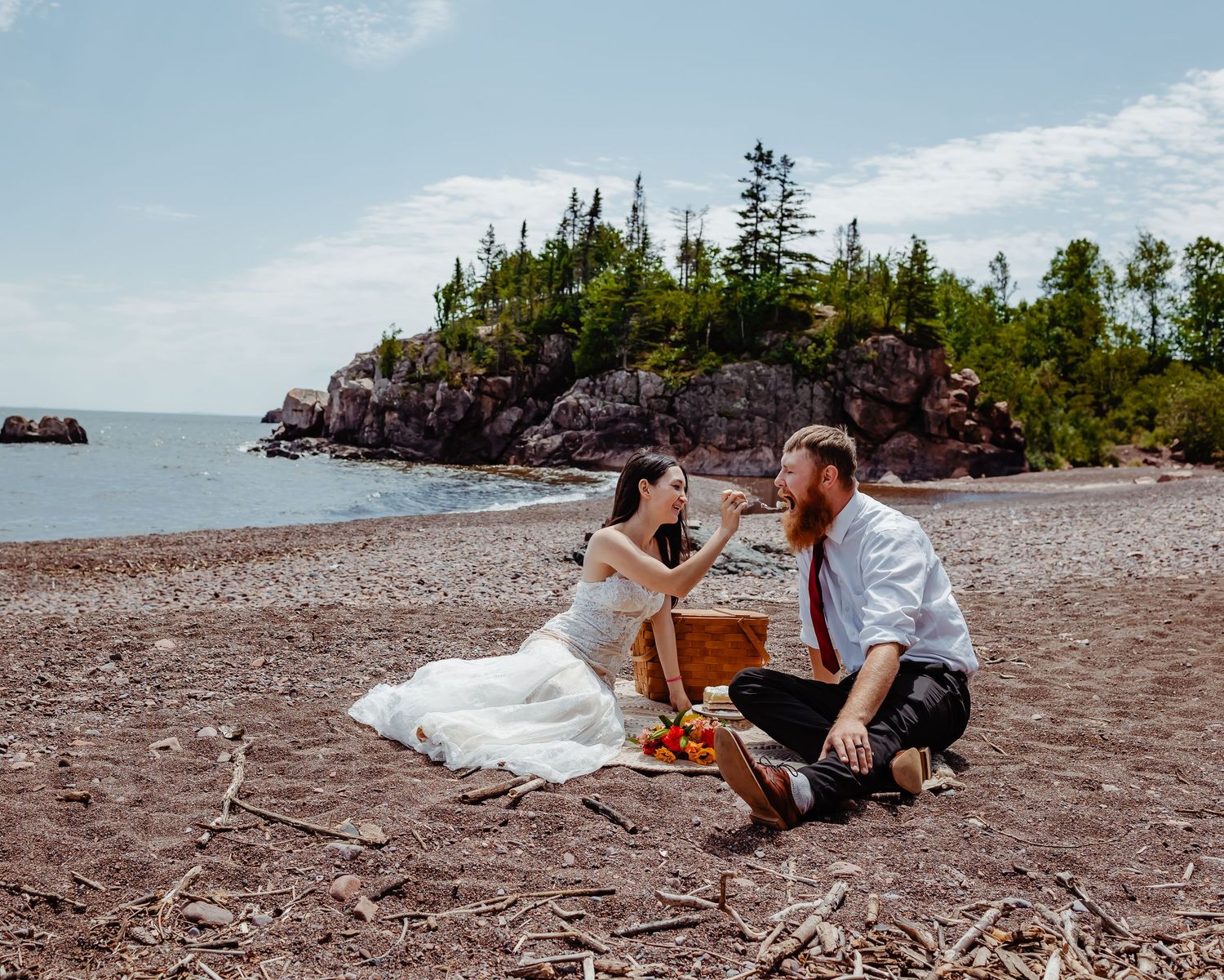 A romantic picnic scene on a rocky beach with evergreen-covered cliffs.
