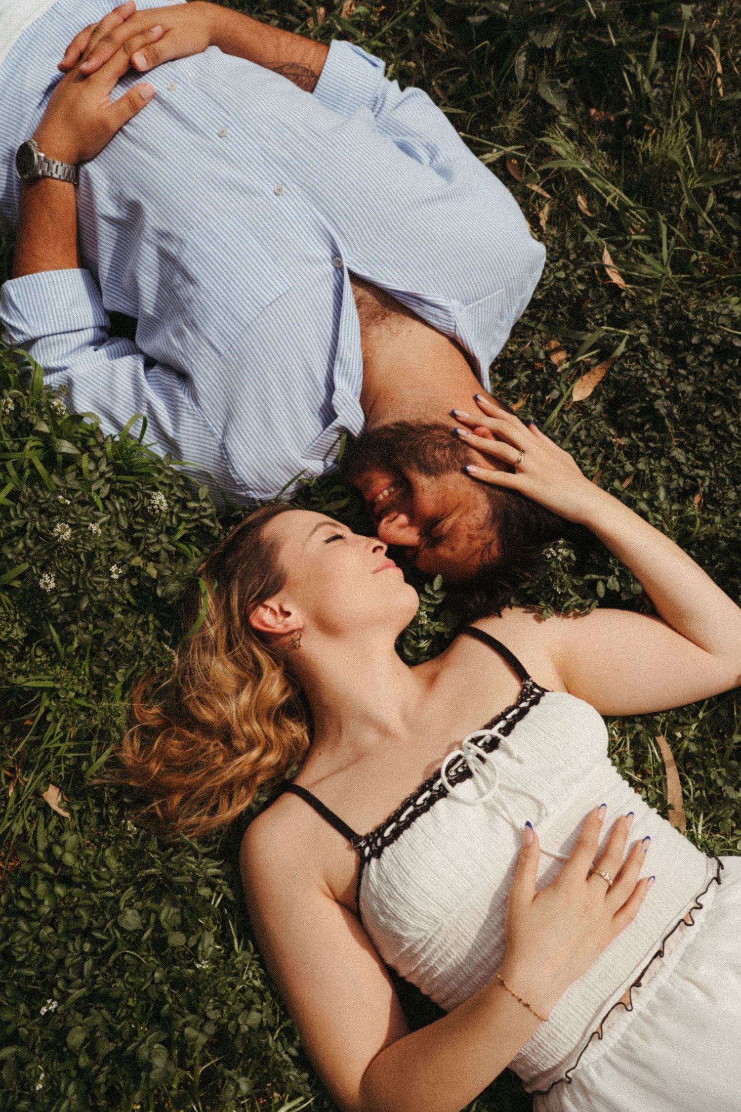 Couple lying together on grass in romantic outdoor maternity photoshoot.