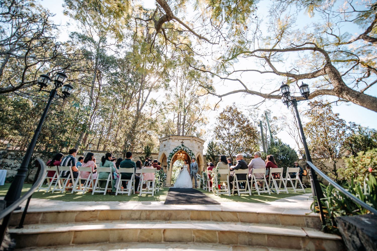 Outdoor wedding ceremony setup with white chairs and natural forest backdrop on elevated stone platform.