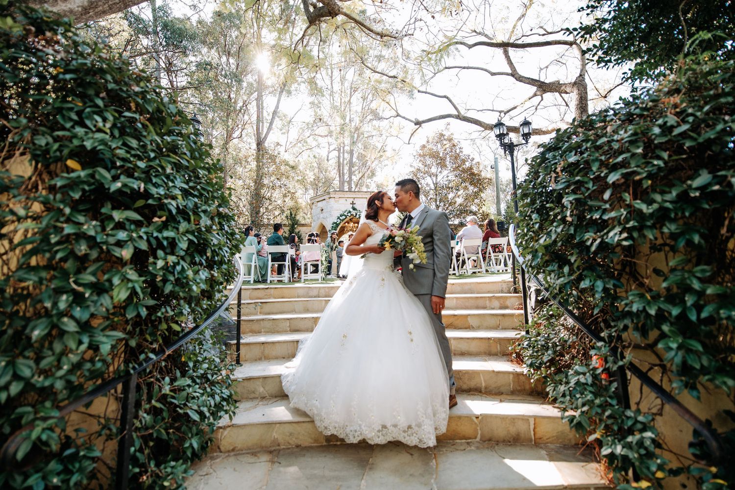 Newlyweds embrace while ascending garden steps lined with ivy.