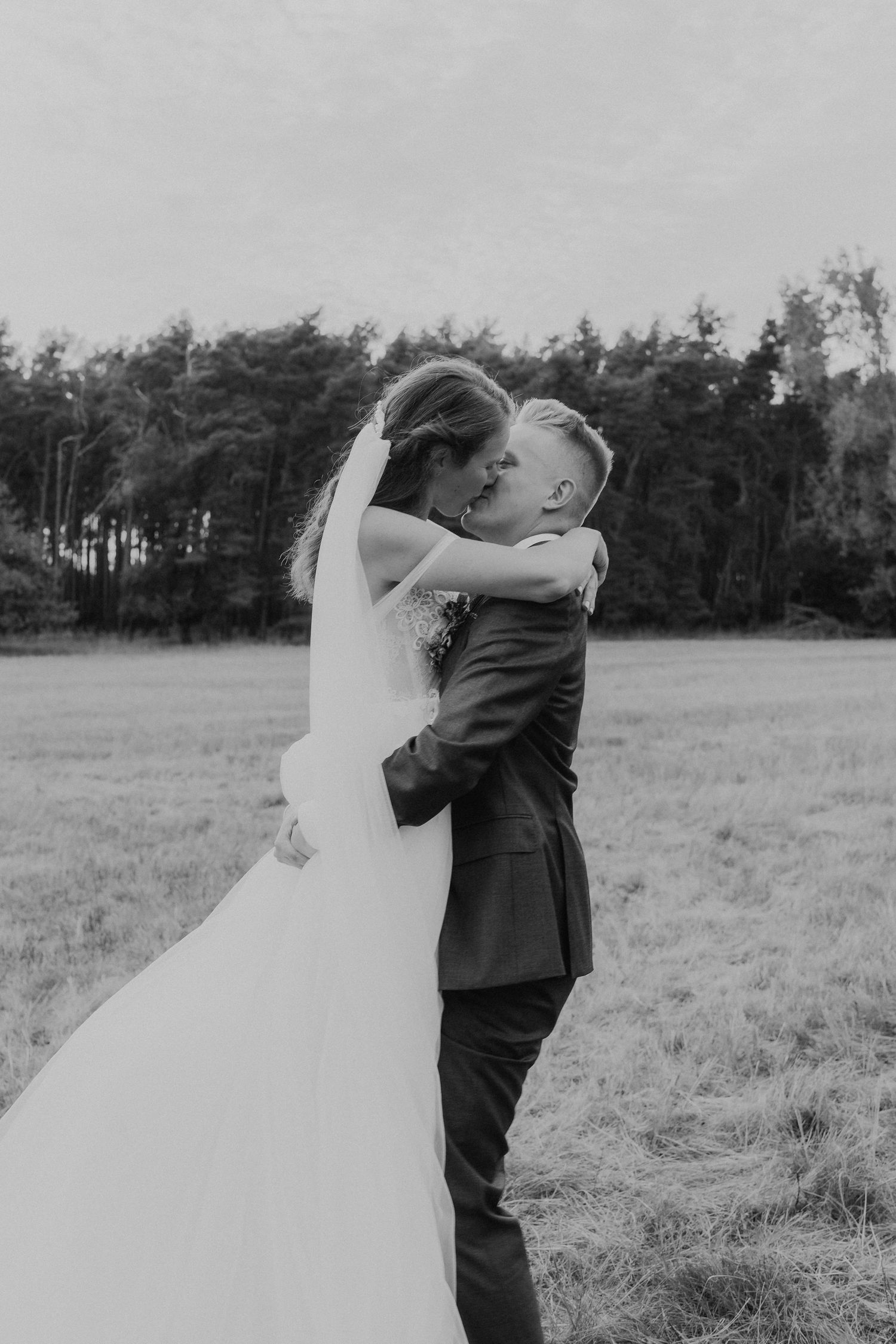 A romantic black and white wedding photo of a couple embracing in a field.