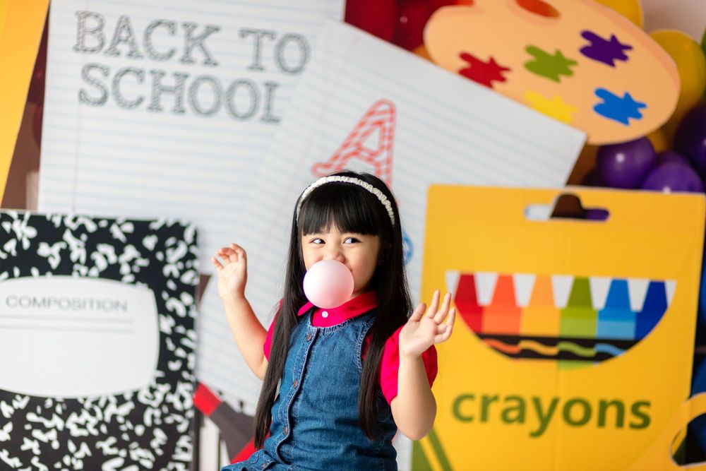 A student in denim jumper shows excitement against a background with crayons and school supplies.