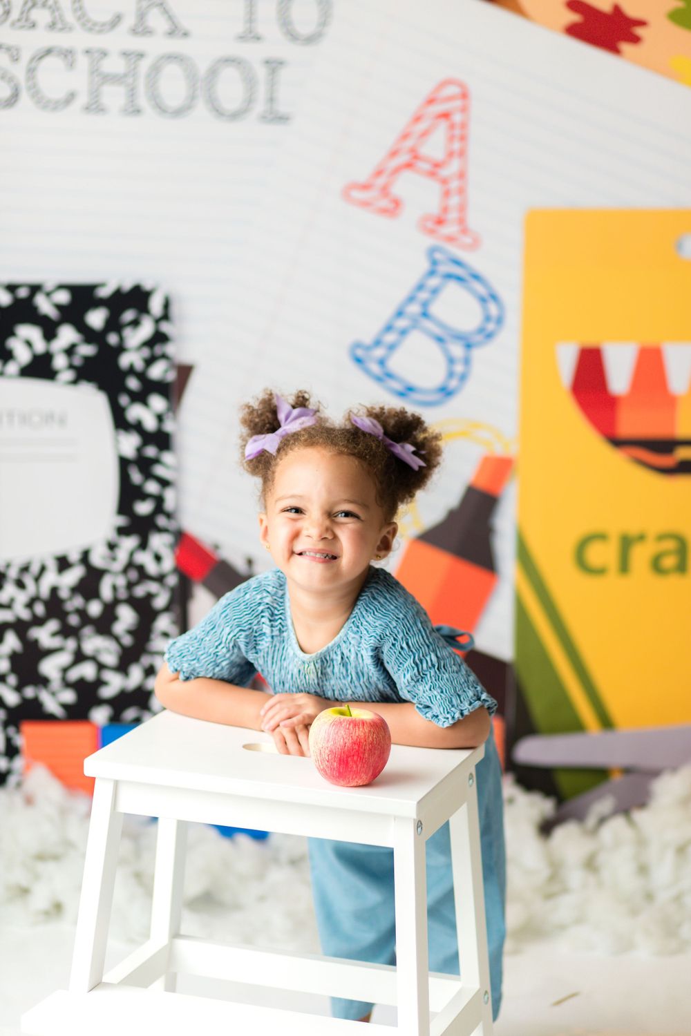 A student sits at a white desk with an apple and school supplies against a decorative background.