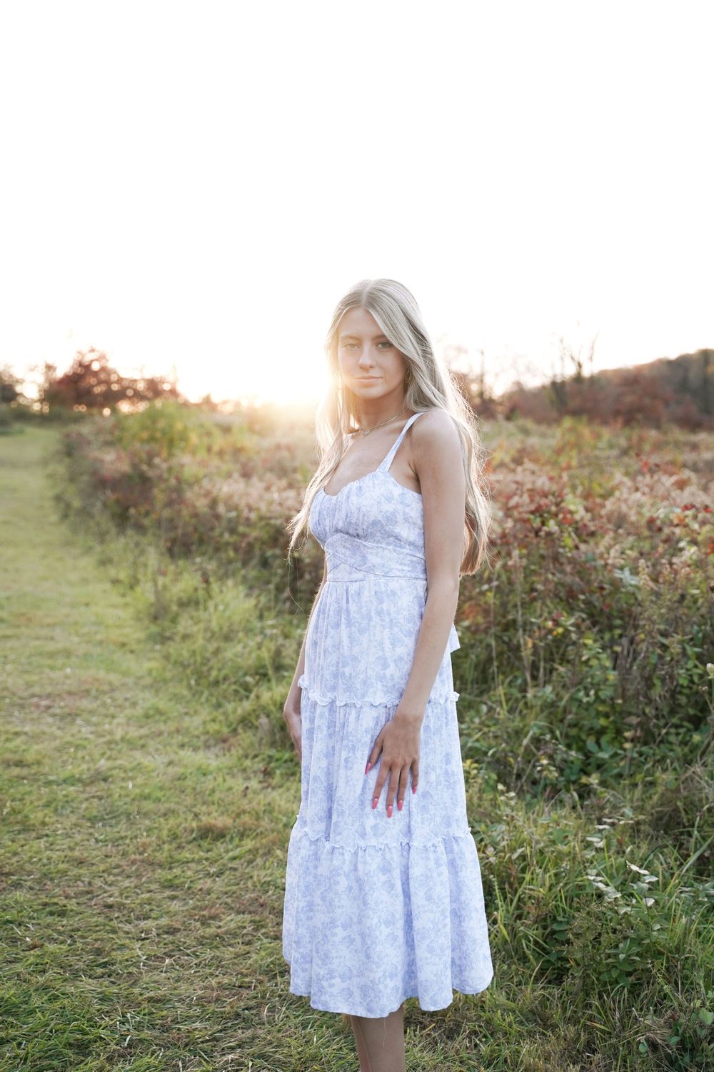 White floral summer dress styled against a golden-lit meadow backdrop.