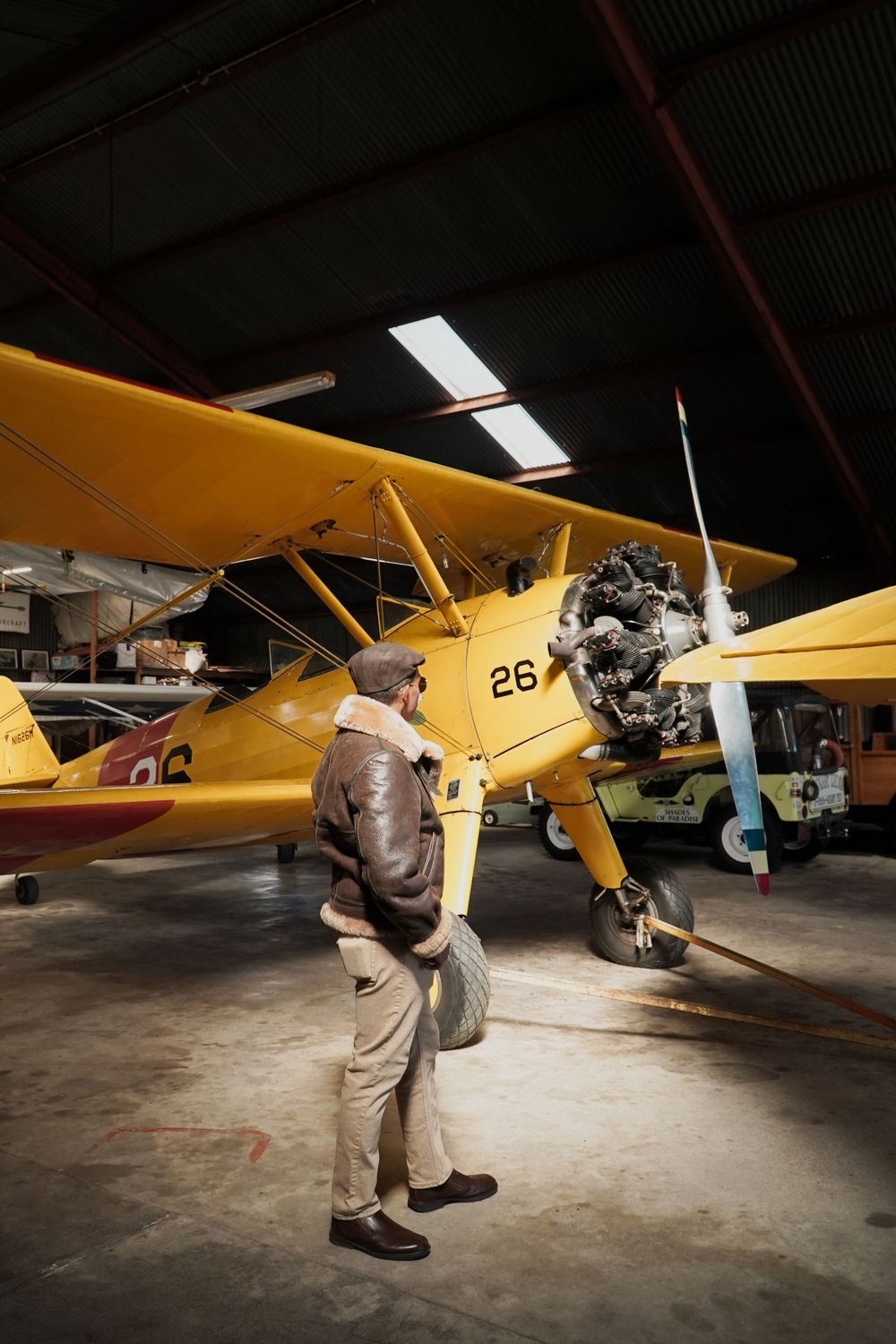 Person examining classic yellow biplane in dimly lit aircraft hangar.