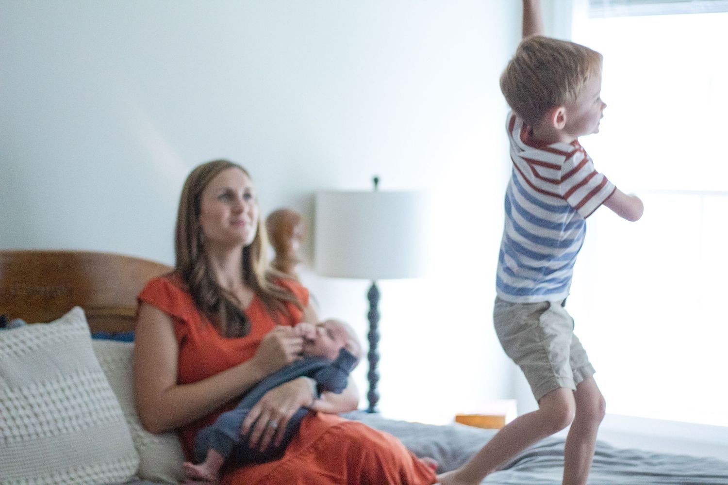 Family Lifestyle: Mom holding baby on bed, while toddler dances on bed.