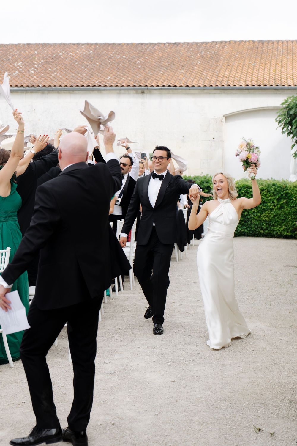 Joyful bride and groom walk down the aisle as guests celebrate at an elegant outdoor wedding ceremony.