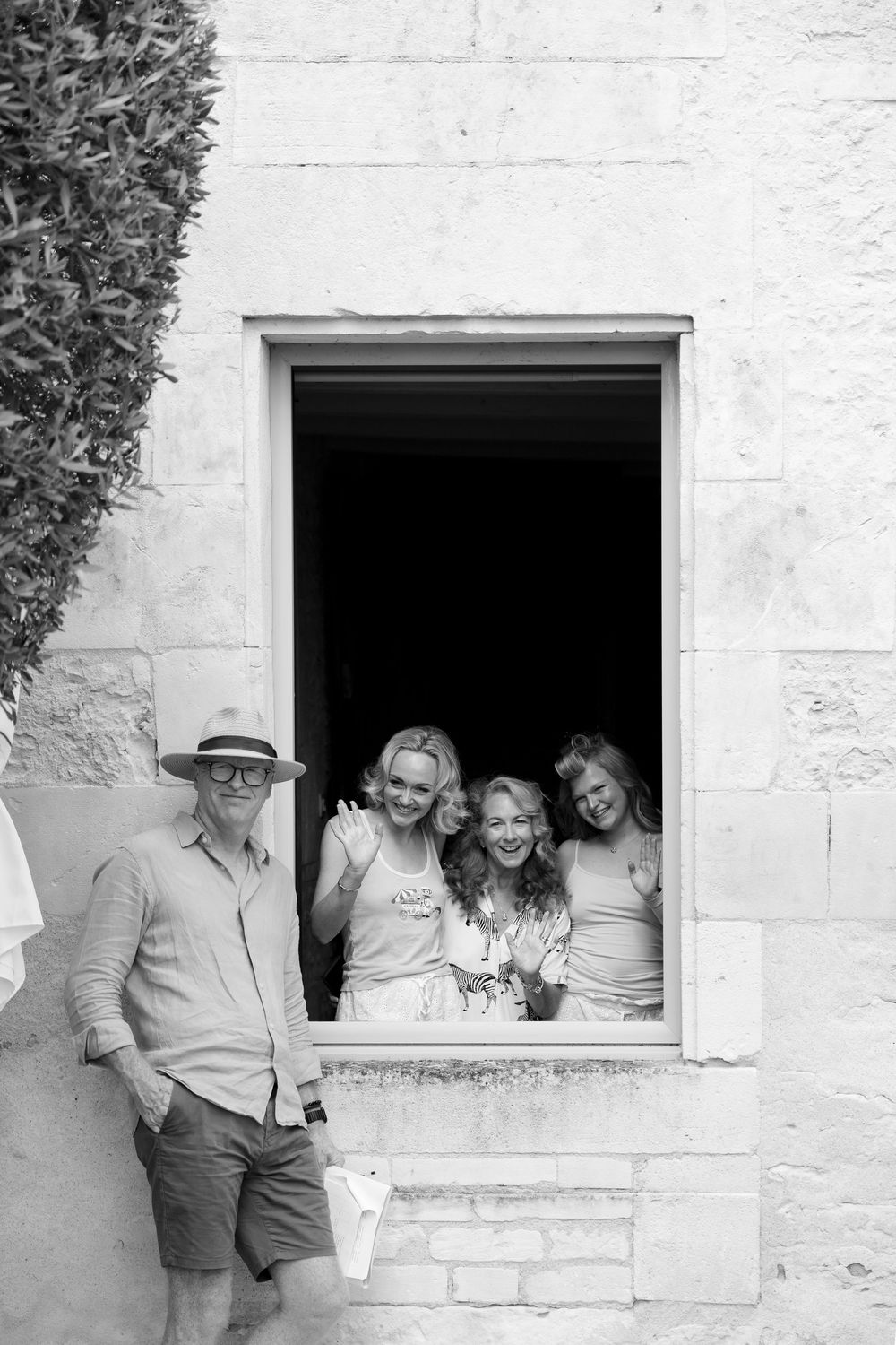 Black and white photo of a man in a hat and three women smiling from an open stone building window.