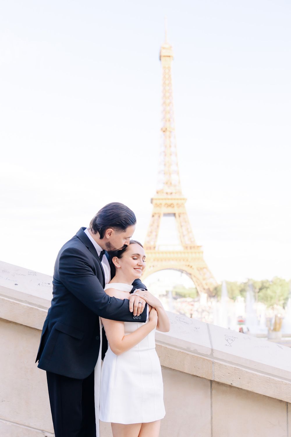 A romantic couple shares tender moments with the Eiffel Tower in Paris visible in the background.