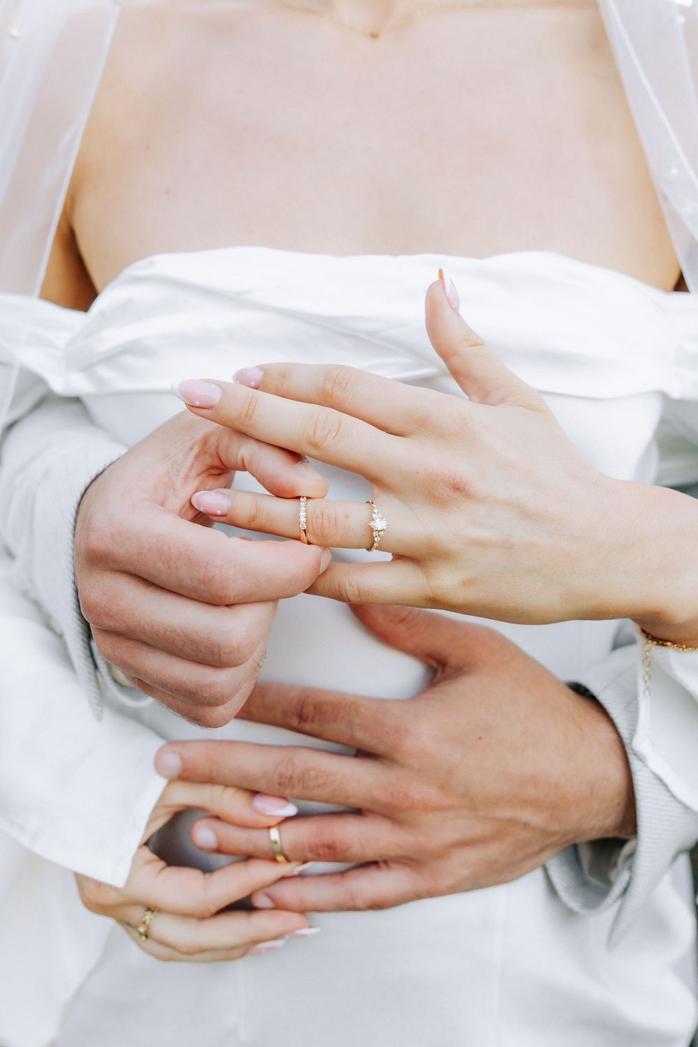 Close-up of hands with wedding rings and soft white fabric showing delicate details of jewelry.